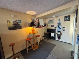 A room with a small bar area featuring stools, a table with a lamp, and various posters on the walls.