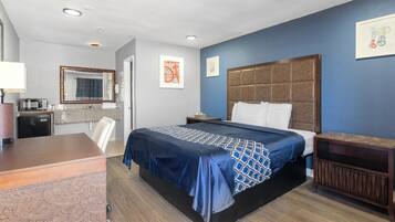 Habitación de hotel con una cama, un escritorio, un aparador, un espejo y una pequeña kitchenette.