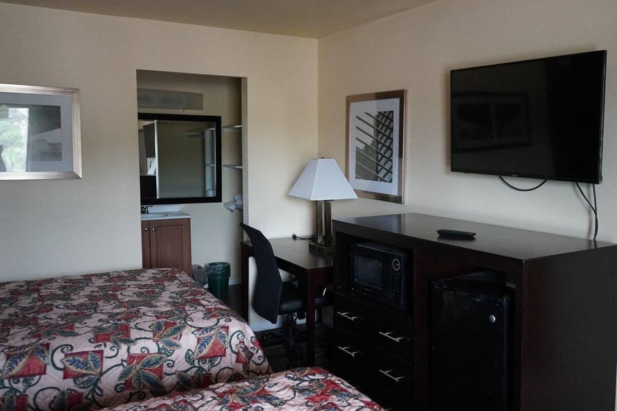 A hotel room with a bed, desk, TV, and a small kitchenette.
