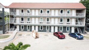 A multi-story building with balconies, a parking area, and a small garden. - Village Motor Inn (Austin)