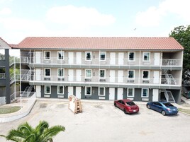 A multi-story building with balconies, a parking area, and a small garden.