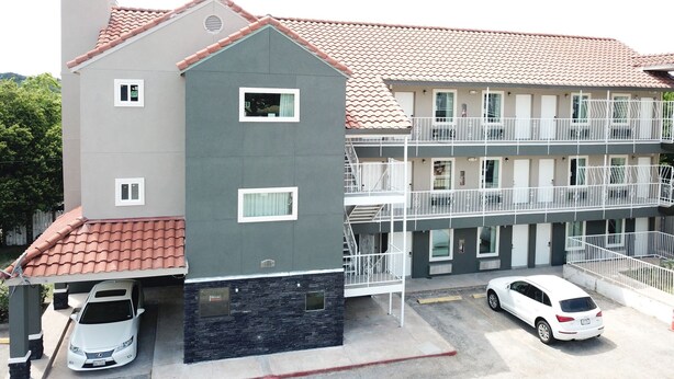 A multi-story building with a red-tiled roof, a covered parking area, and a white car parked in the driveway. - Village Motor Inn (Austin)