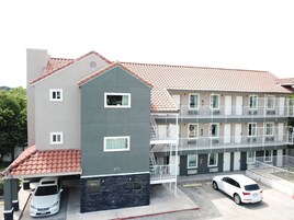 A multi-story building with a red-tiled roof, a covered parking area, and a white car parked in the driveway.