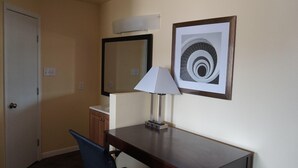 A hotel room with a desk, chair, lamp, and two framed pictures on the wall. - Village Motor Inn (Austin)
