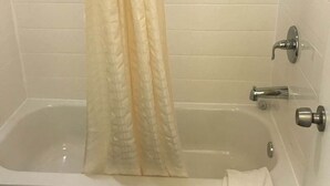 A bathroom with a bathtub, a shower curtain, and a towel on the floor. - Village Motor Inn (Austin)