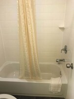 A bathroom with a bathtub, a shower curtain, and a towel on the floor.