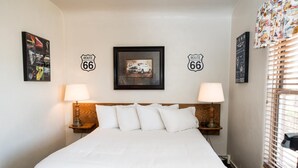 A hotel room with a large bed, two bedside lamps, a headboard, and Route 66 themed decorations on the walls. - Historic Route 66 Motel (Seligman)