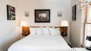 Une chambre d’hôtel avec un grand lit, deux lampes de chevet, une tête de lit et des décorations sur les murs sur le thème de la Route 66.