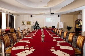 A conference room with a long table, chairs, a projector screen, and a Christmas tree.