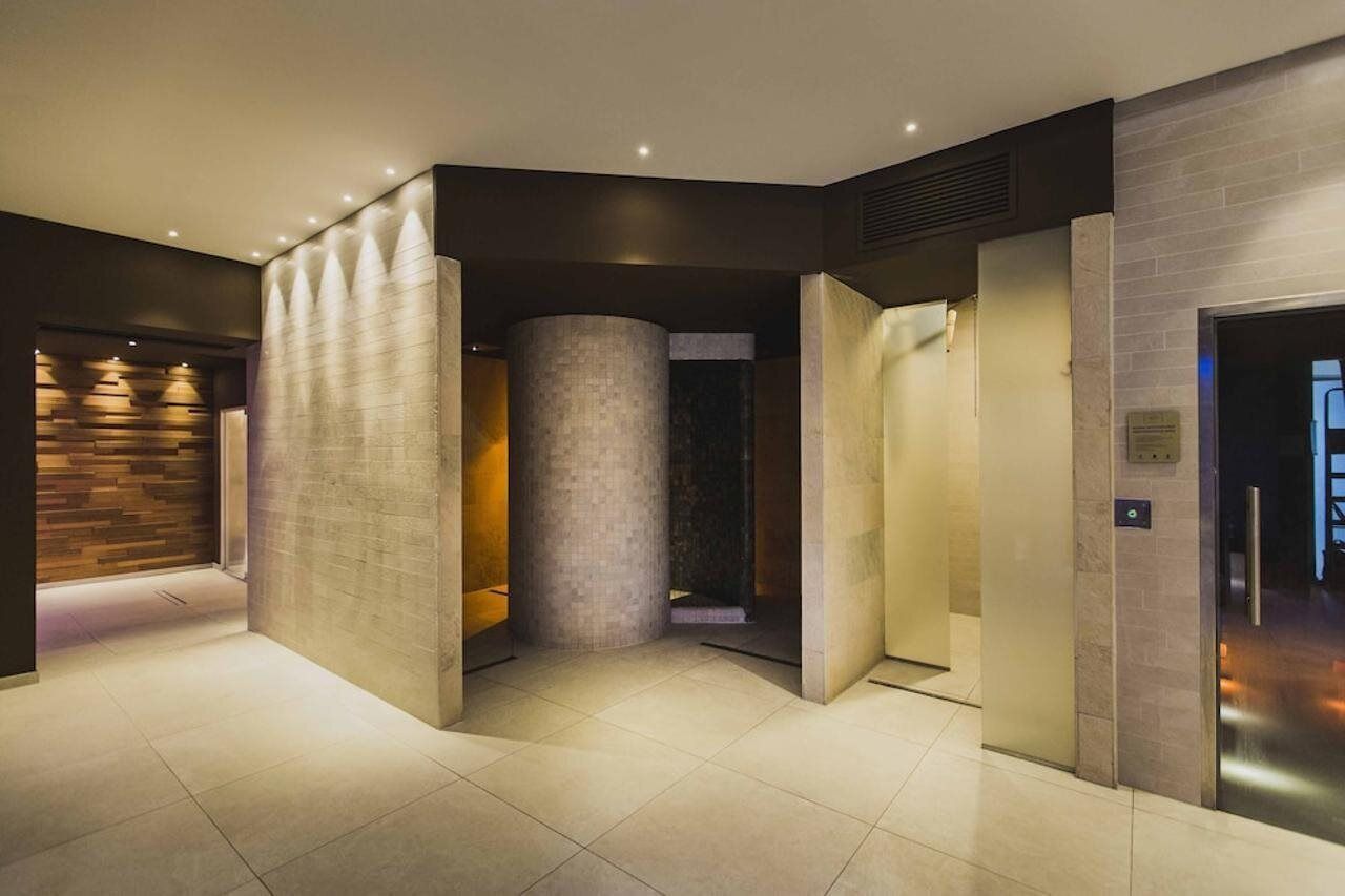 Hall d'hotel moderna con una colonna centrale, illuminazione a scomparsa e un mix di texture in legno e pietra.