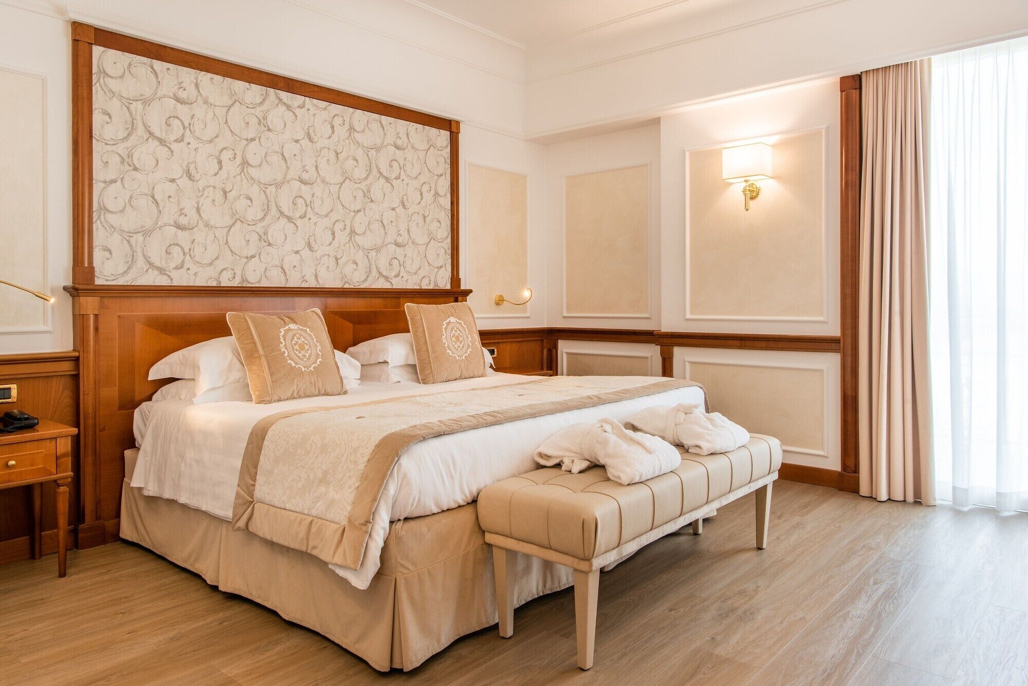 Una camera d'albergo con un letto grande, una panca, un comodino e una parete con un pannello decorativo.