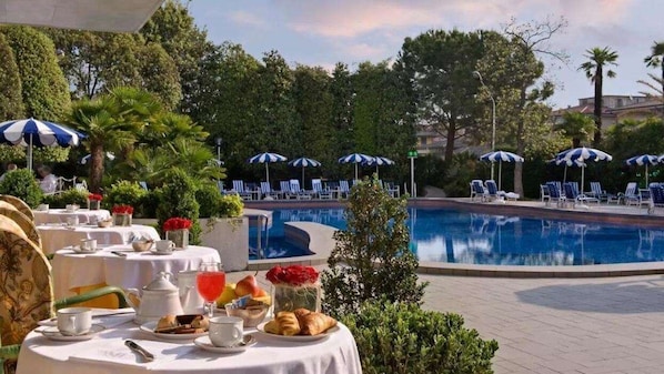 A poolside dining area with tables, chairs, and umbrellas.