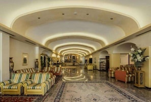 A spacious lobby with a high ceiling, a central staircase, and a seating area with sofas and armchairs.