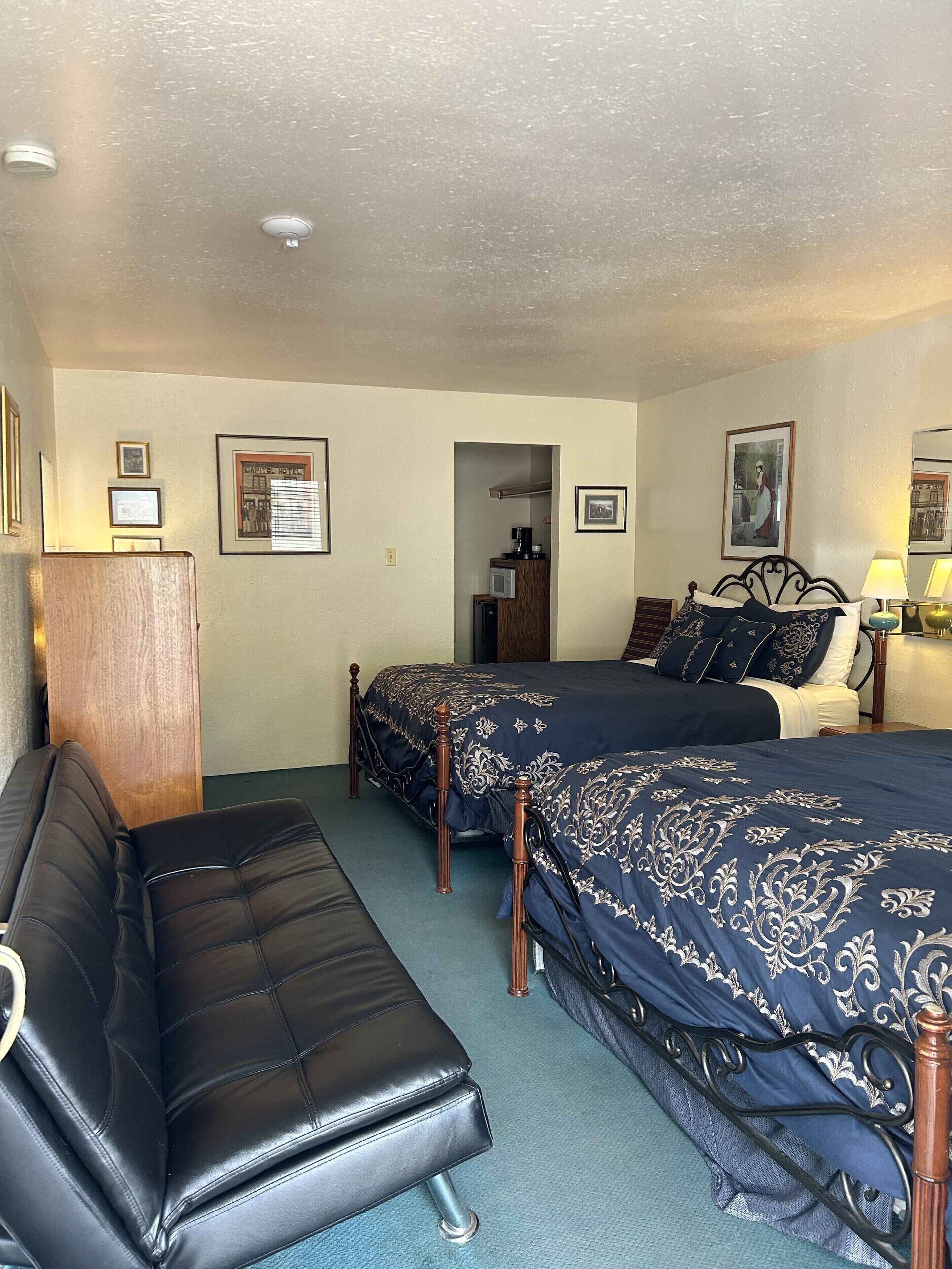 A hotel room with two beds, a sofa, and a kitchenette.