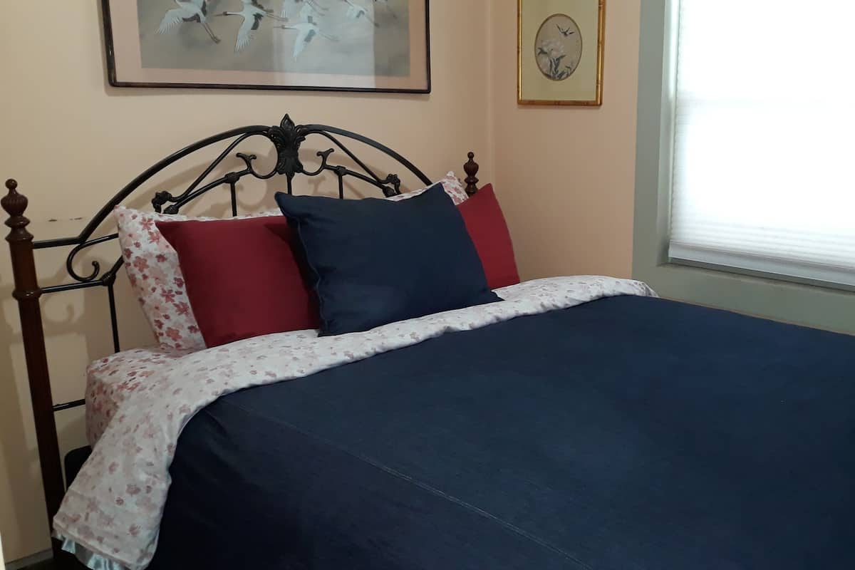 A bed with a floral-patterned bedspread, a dark blue blanket, and two pillows (one red and one blue).