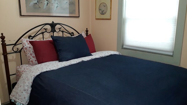 Uma cama com colcha estampada de flores, manta azul escura e dois travesseiros, um vermelho e um azul.