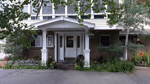 A two-story building with a white front porch, a brick facade, and a small garden area with various plants and flowers. - Columbine INN (Idaho Springs)