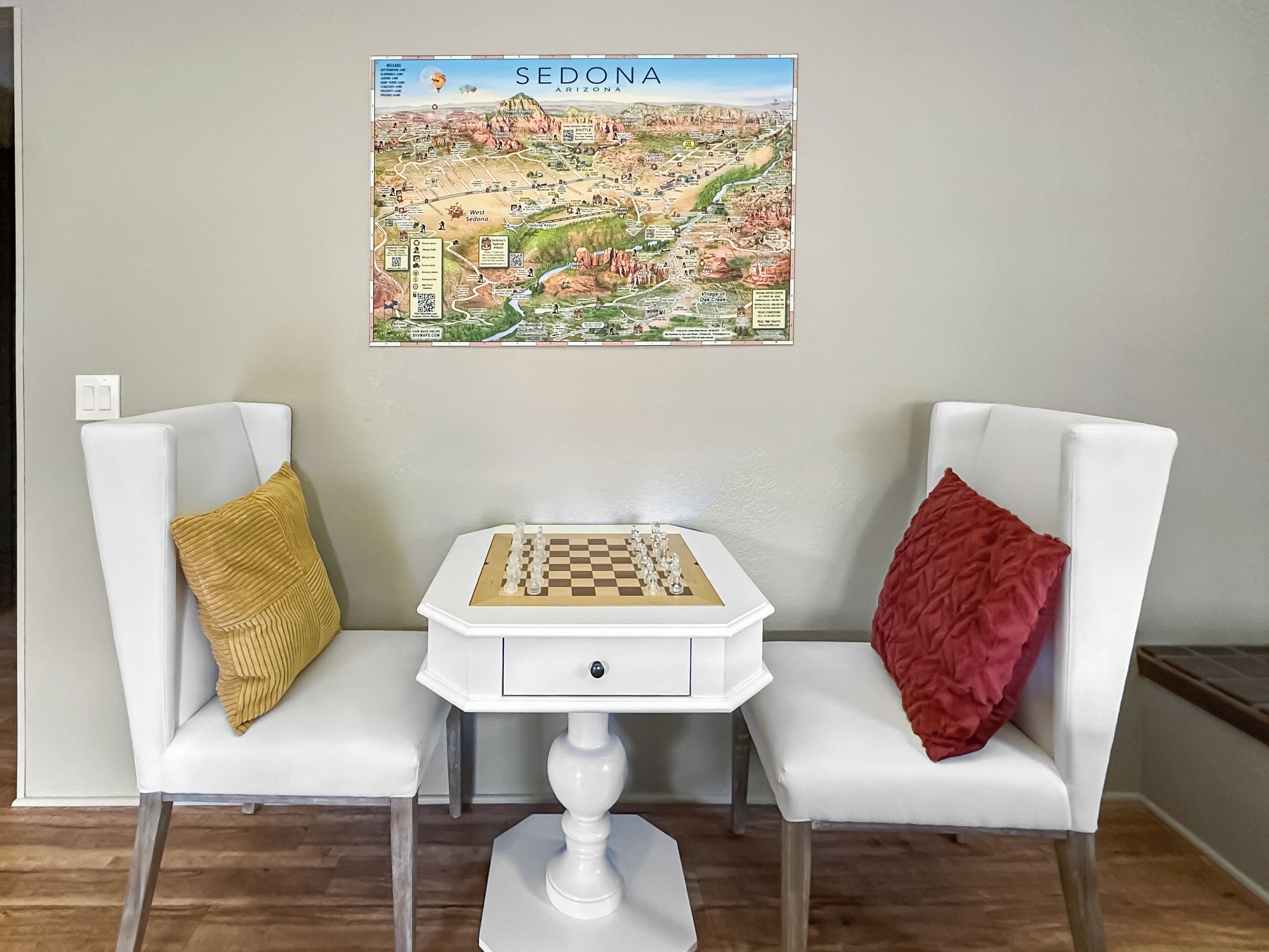 Una habitación con dos sillas blancas, una pequeña mesa blanca con un tablero de ajedrez, y un mapa de Sedona, Arizona en la pared.