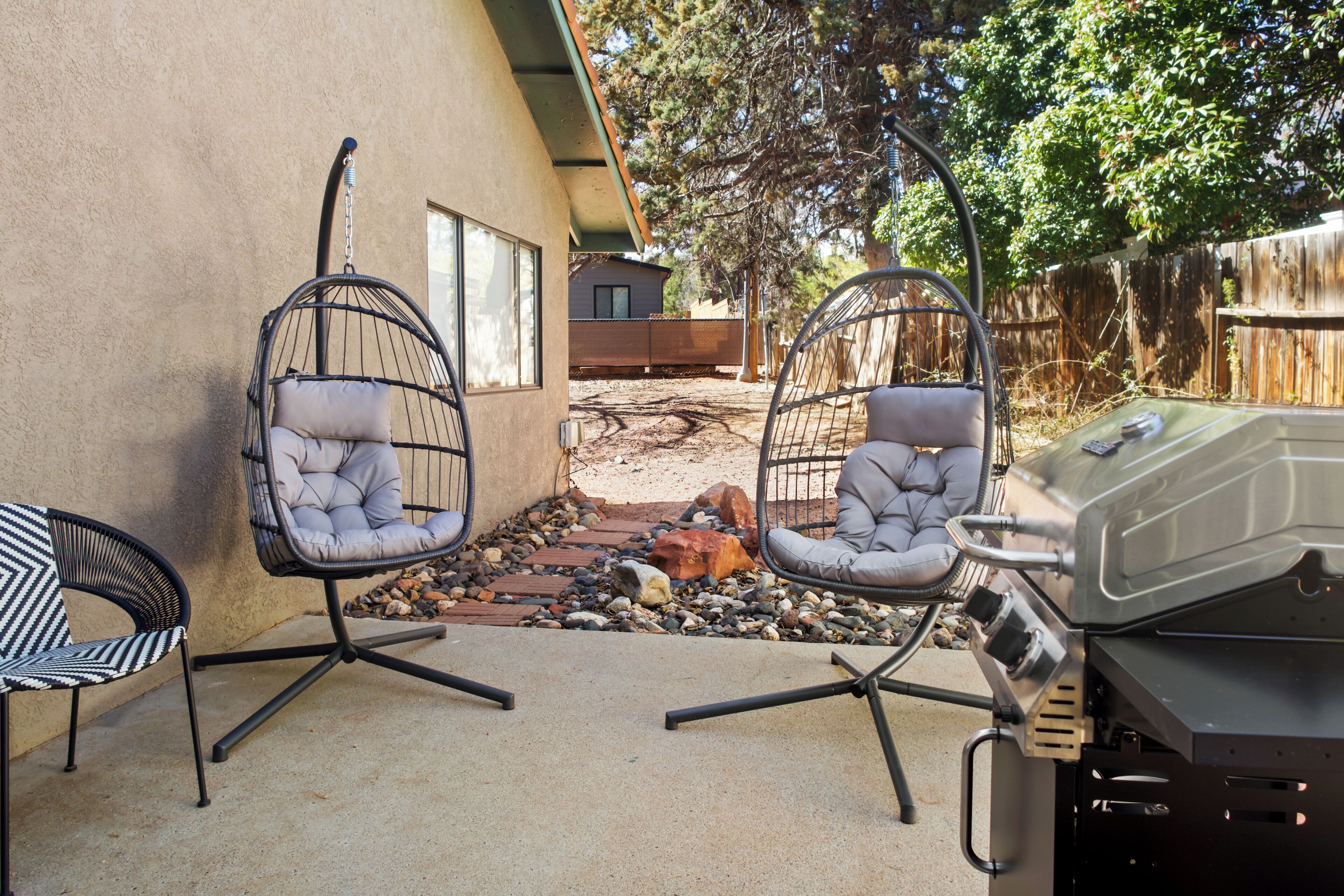 A patio with two hanging chairs, a grill, and a stone pathway.