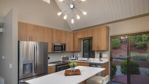 A modern kitchen with stainless steel appliances, wooden cabinets, a central island, and a view of a landscaped garden. - Matterhorn Inn (Sedona)