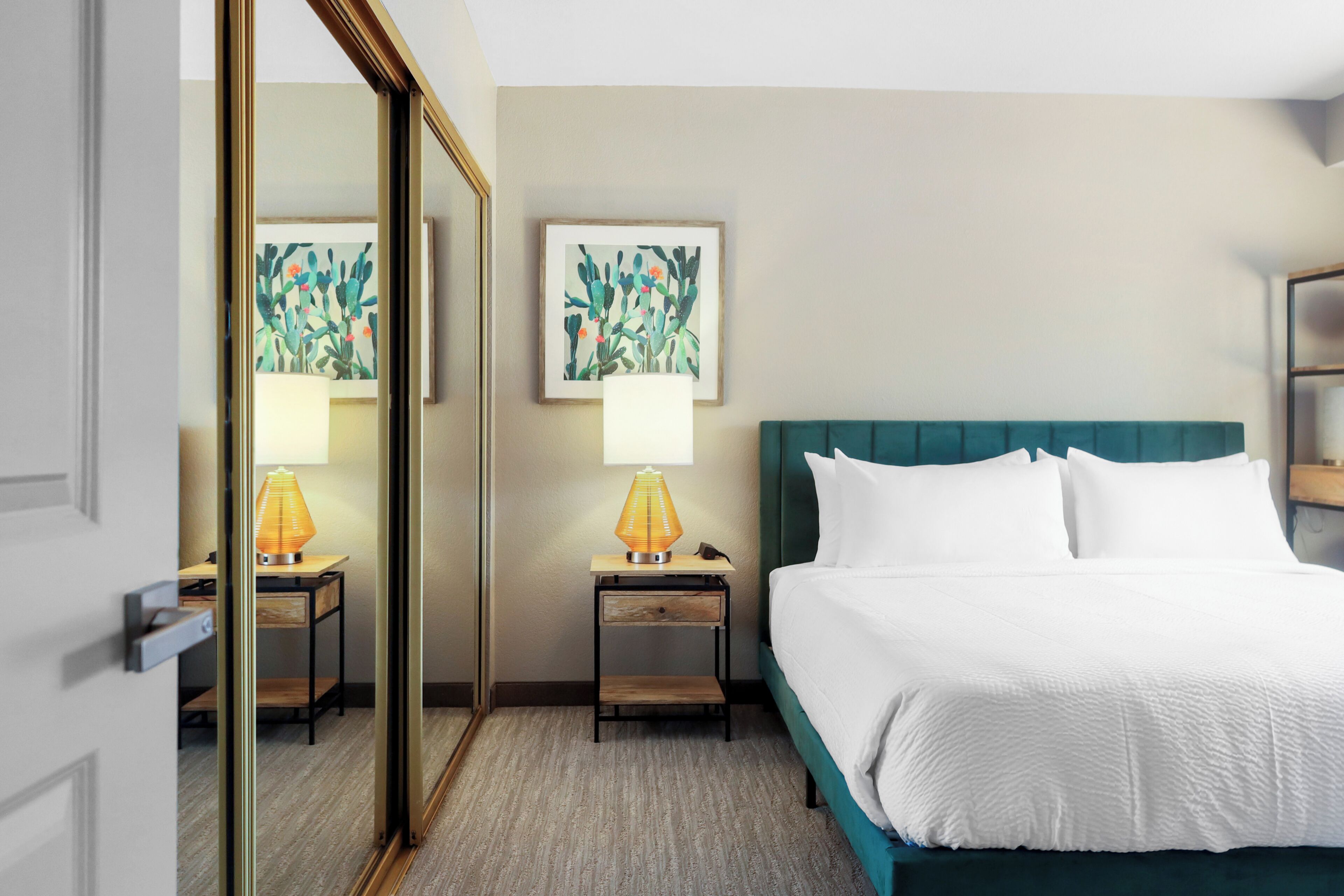 A hotel room with a bed, two nightstands with lamps, a mirror, and two framed artworks on the wall.