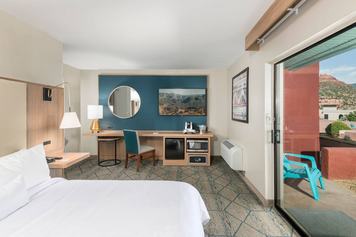 A hotel room with a bed, desk, chair, and a view of the outside.