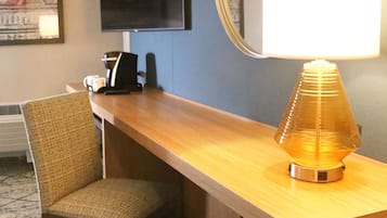 Habitación de hotel con un escritorio de madera, una silla, un televisor montado en la pared y un espejo.