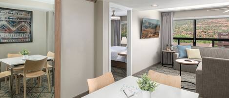 A hotel room with a dining area, a sofa, and a view of a mountainous landscape.