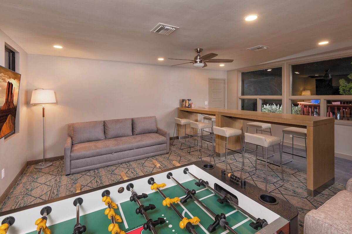 Une pièce équipée d’un baby-foot, d’un canapé, d’un coin bar avec des tabourets et d’un ventilateur de plafond.