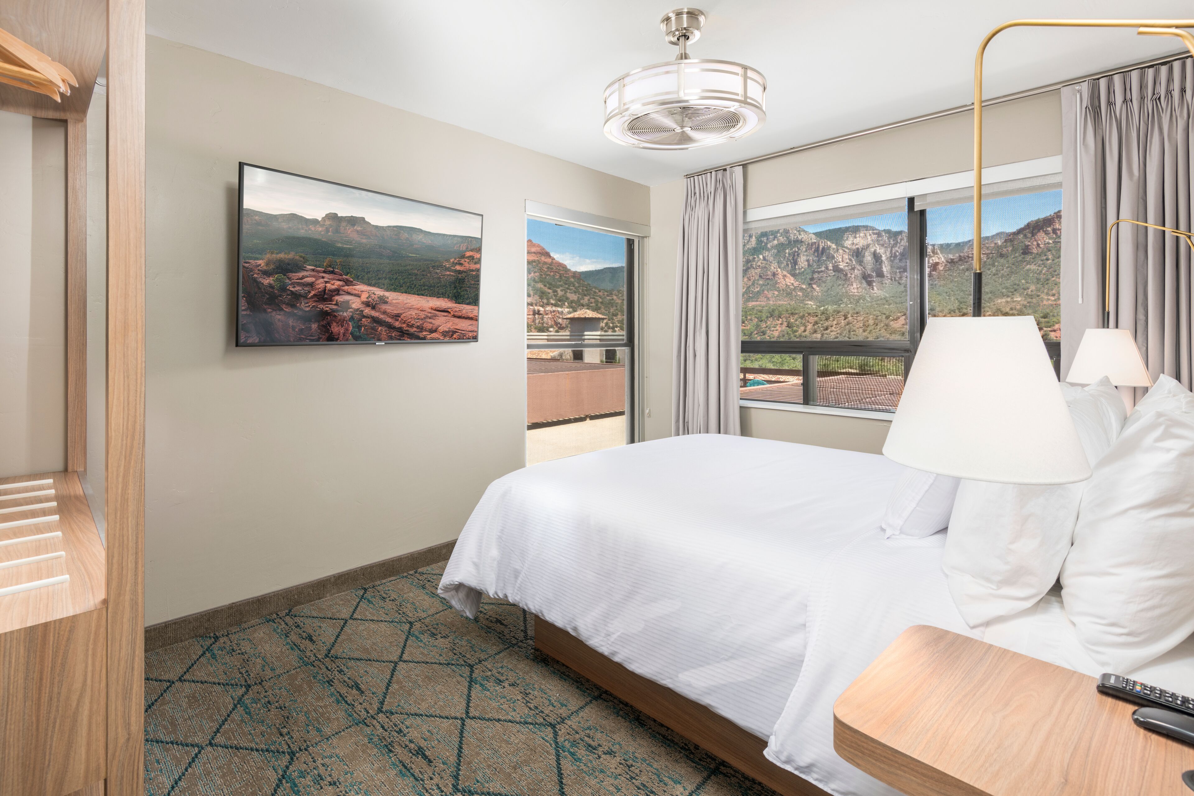 Une chambre d’hôtel avec un lit, un téléviseur fixé au mur, une fenêtre avec des rideaux et une vue sur les montagnes.