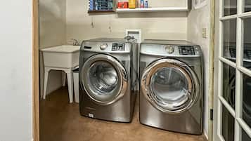 A laundry room with two front-loading washing machines, a small sink, and a window with blinds.
