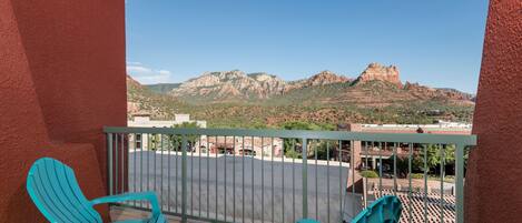 A balcony with turquoise chairs and a table, overlooking a parking area and mountains.