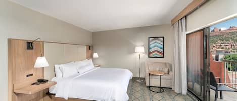 A hotel room with a bed, bedside tables, a chair, a small table, and a balcony with a view.