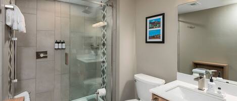 Un baño moderno con ducha de vidrio, inodoro blanco y tocador de madera con lavamanos.