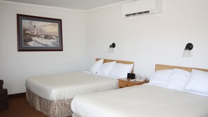 A hotel room with two beds, a painting of a lighthouse, a bedside table with a lamp, and an air conditioning unit on the wall. - The Bluebird Motel (Machias)