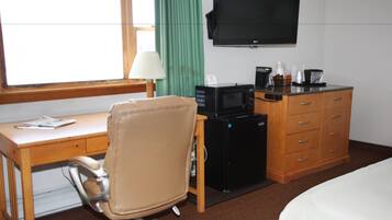 Habitación de hotel con escritorio de madera, sillón de cuero, televisor, minibar y cama.