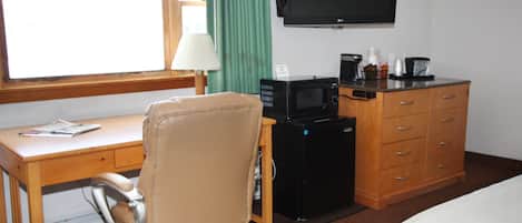 Habitación de hotel con escritorio de madera, sillón de cuero, televisor, minibar y cama.
