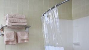 A bathroom with a bathtub, a shower curtain, and towels on a rack. - The Bluebird Motel (Machias)