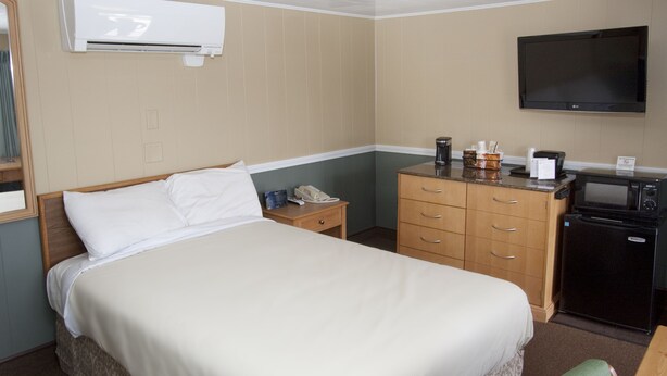 A hotel room with a bed, a nightstand, a dresser, a microwave, and a television. - The Bluebird Motel (Machias)