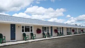 A motel with a row of rooms, each with a door and windows, and a covered outdoor seating area with chairs. - The Bluebird Motel (Machias)