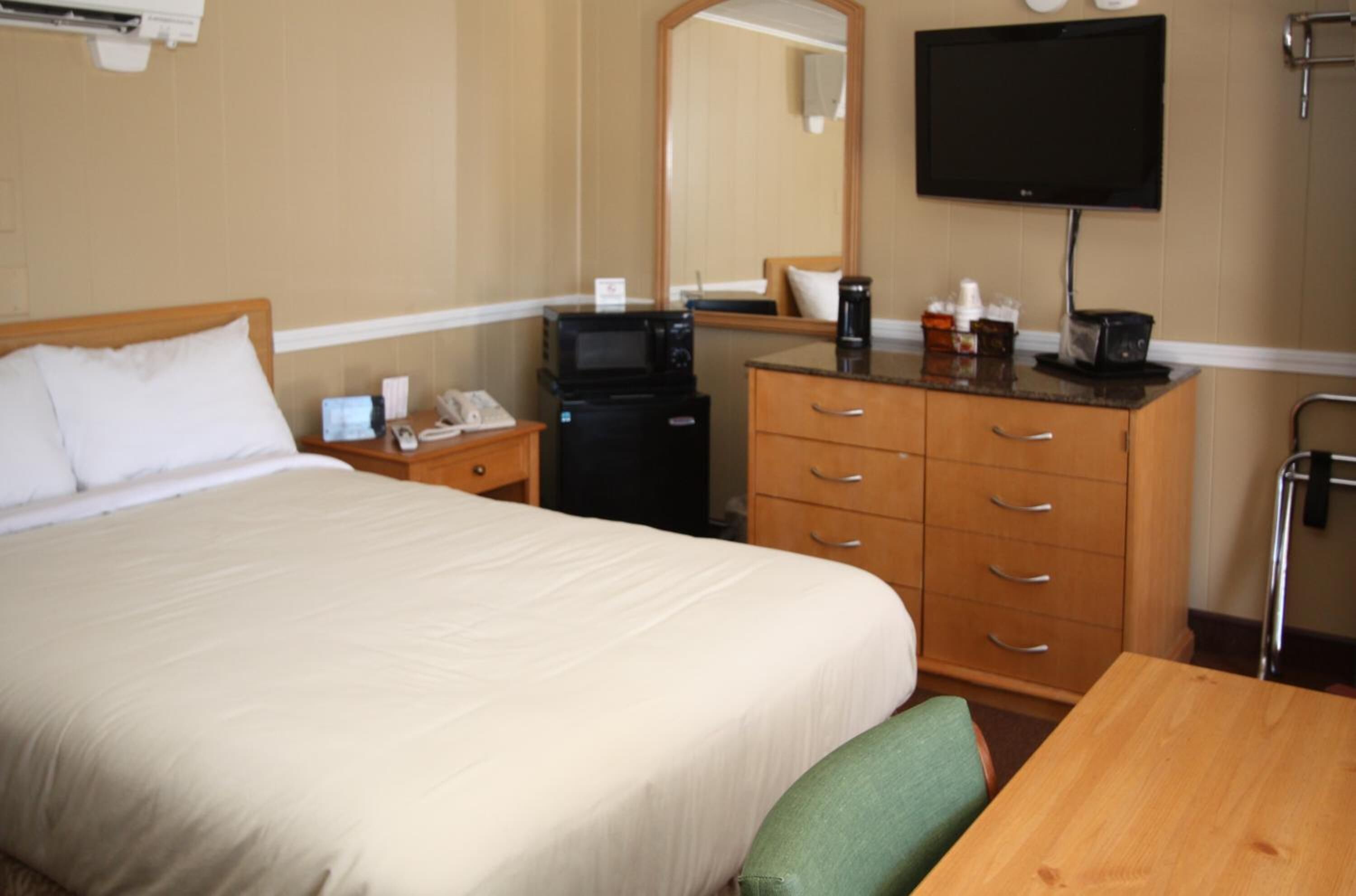 A hotel room with a large bed, a desk, a microwave, a coffee maker, and a TV.