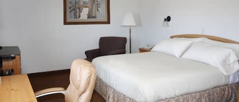 Et hotelværelse med en seng, et skrivebord, en stol, en lampe og et billede i ramme på væggen.