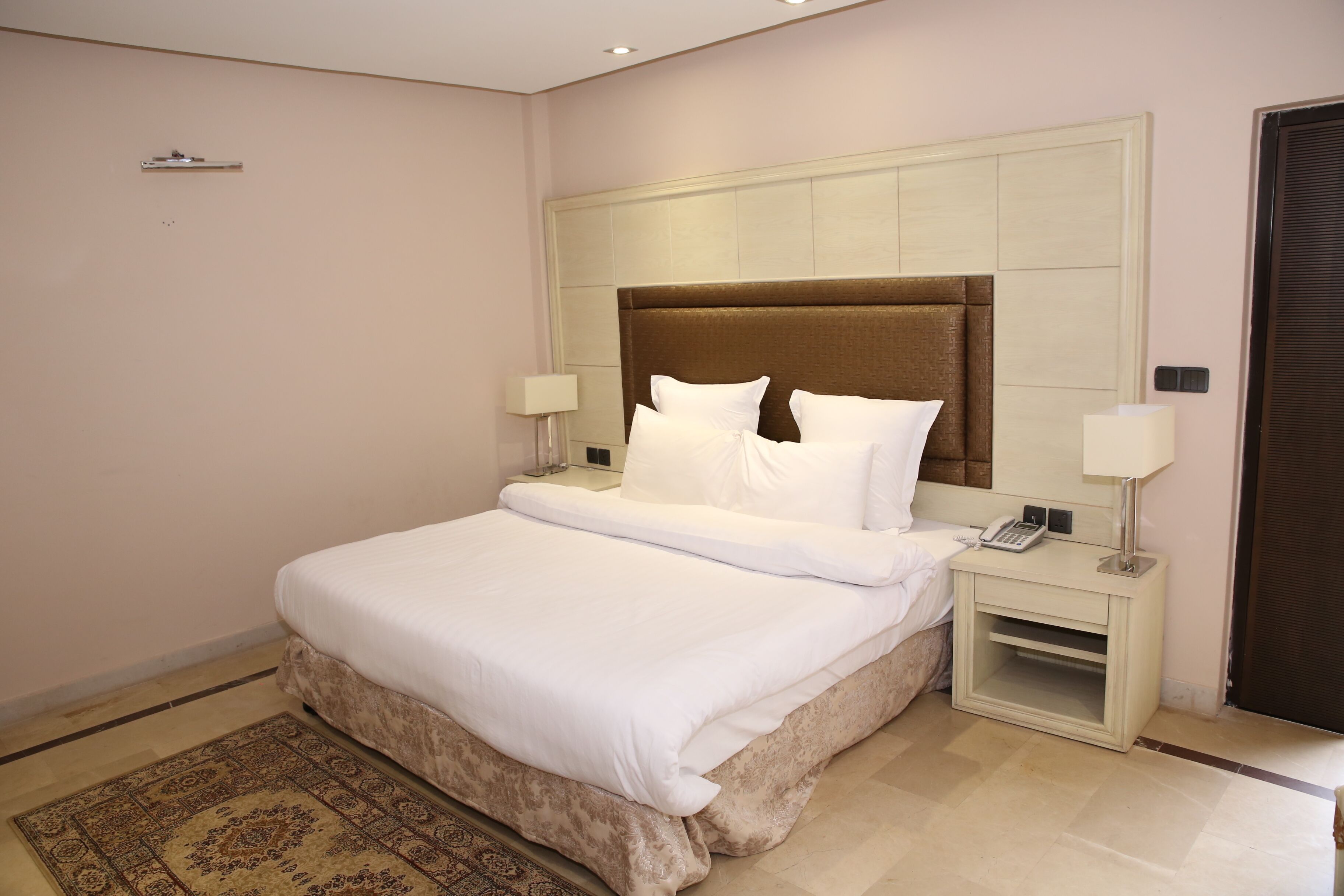 Un cuarto de hotel ordenado con una cama grande, mesitas de noche y una alfombra estampada.