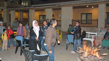 An outdoor seating area with a fire pit, chairs, and a building with a balcony in the background.