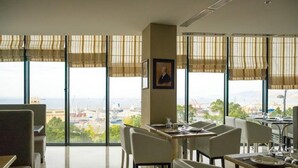 Un espace repas doté de grandes fenêtres, offrant une vue sur la ville, et orné d’un portrait encadré au mur.