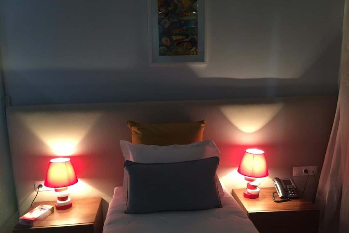 Une chambre d’hôtel avec un lit, deux tables de chevet avec des lampes, un téléphone et un tableau au mur.