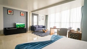 Une chambre d’hôtel moderne dotée d’un grand lit, d’un téléviseur à écran plat, d’un canapé, d’un bureau et d’une grande fenêtre.