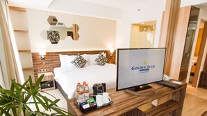 Habitació d'hotel amb un llit, televisió, escriptori de fusta i una planta.