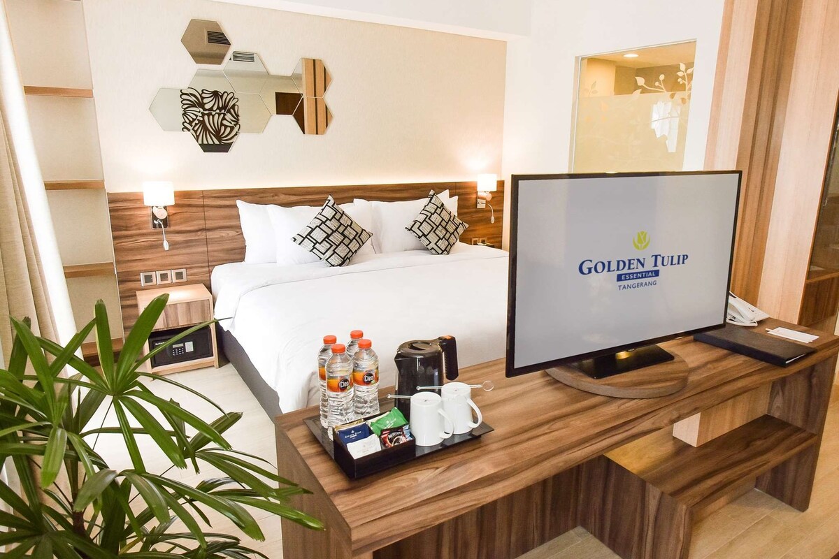 A hotel room with a bed, bedside table with a TV, a coffee maker, and a tray with bottled water and a coffee cup.