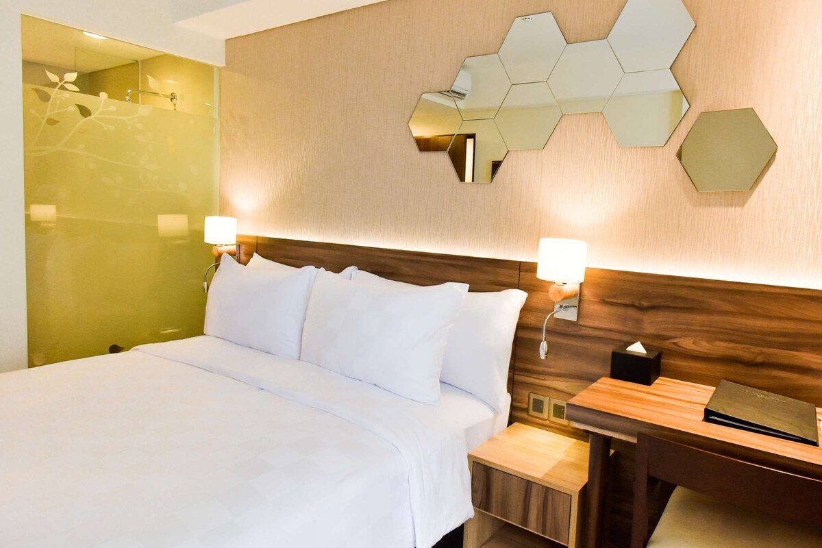 A hotel room with a large bed, two bedside tables, a nightstand, a mirror, and a wall with a geometric pattern.
